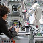 Engineer holding a teach panel to control a robotic arm